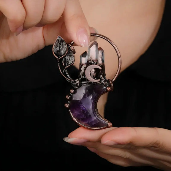 Hand holding natural amethyst crescent moon celestial pendant
