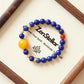 Astral Orbit Zenith AI Companion Bracelet displayed on Zenstellar presentation card with warm ambient lighting highlighting Lapis Lazuli and Red Agate gemstone design