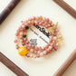 Auric Hue Crest AI Companion Bracelet displayed on Zenstellar presentation card with warm ambient lighting highlighting Orange Moonstone and Phantom Quartz crystal energy design