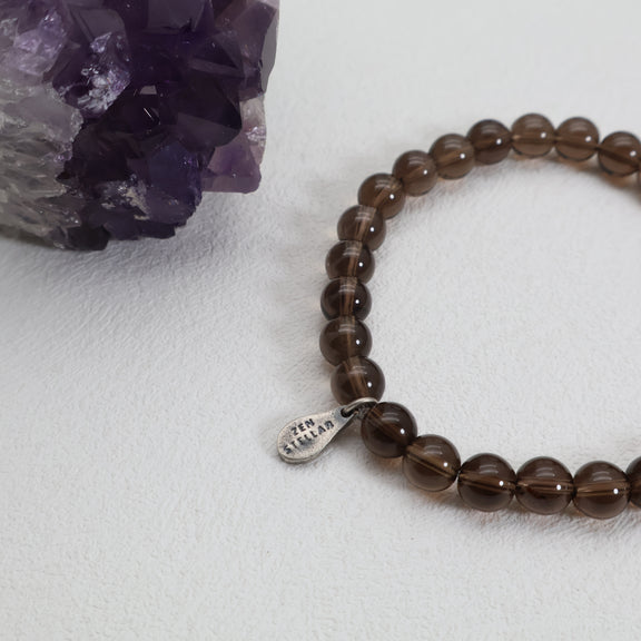 Close-up of smoky quartz beads and the ZenStellar silver charm beside a purple crystal cluster.