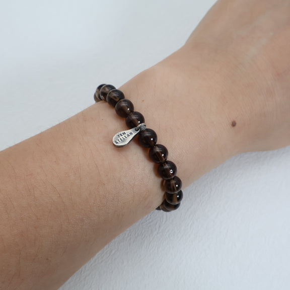 Earthbound Calm smoky quartz bracelet worn on the wrist, showing brown gemstone beads and a ZenStellar silver charm.