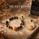 Heart Bond Tiger Eye and Citrine couple bracelets with golden companion beads displayed on a stone pedestal beside a phone.