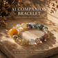 A natural rutilated quartz crystal bracelet displayed on a warm textured stone surface under soft golden sunlight, featuring 10mm multi-tone crystal beads and an orange focal bead, representing a dynamic AI companion bracelet experience with flowing energy and clarity.