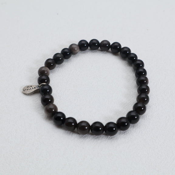 Top view of the Silver Shadow obsidian bracelet with round black beads and a silver charm on a white surface.