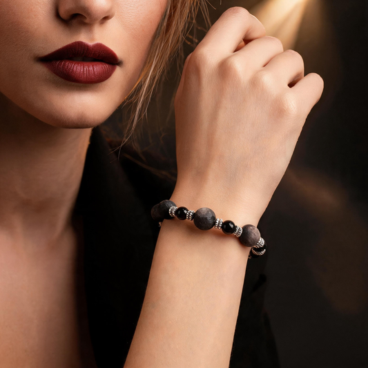 Silver sheen obsidian bracelet worn on the wrist, showing textured dark beads, polished black beads and decorative silver-tone spacers.