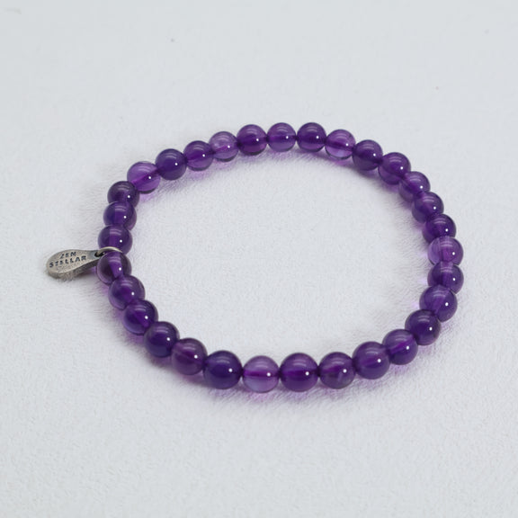 Top view of the Violet Clarity amethyst bracelet with round purple beads and a 925 sterling silver charm on a white surface.